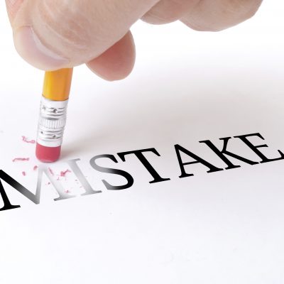 Male hand holding wooden pencil and delete word "MISTAKE" on the white paper